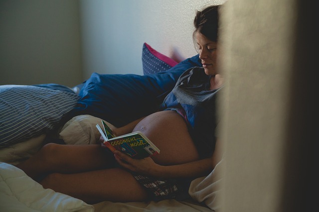 Tehotná žena sedí v posteli, na ktorej sú paplóny a vankúše.jpg
