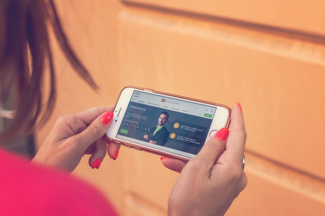 Žena s ružovým nechtami drží v rukách mobil a pozerá na webovú stránku